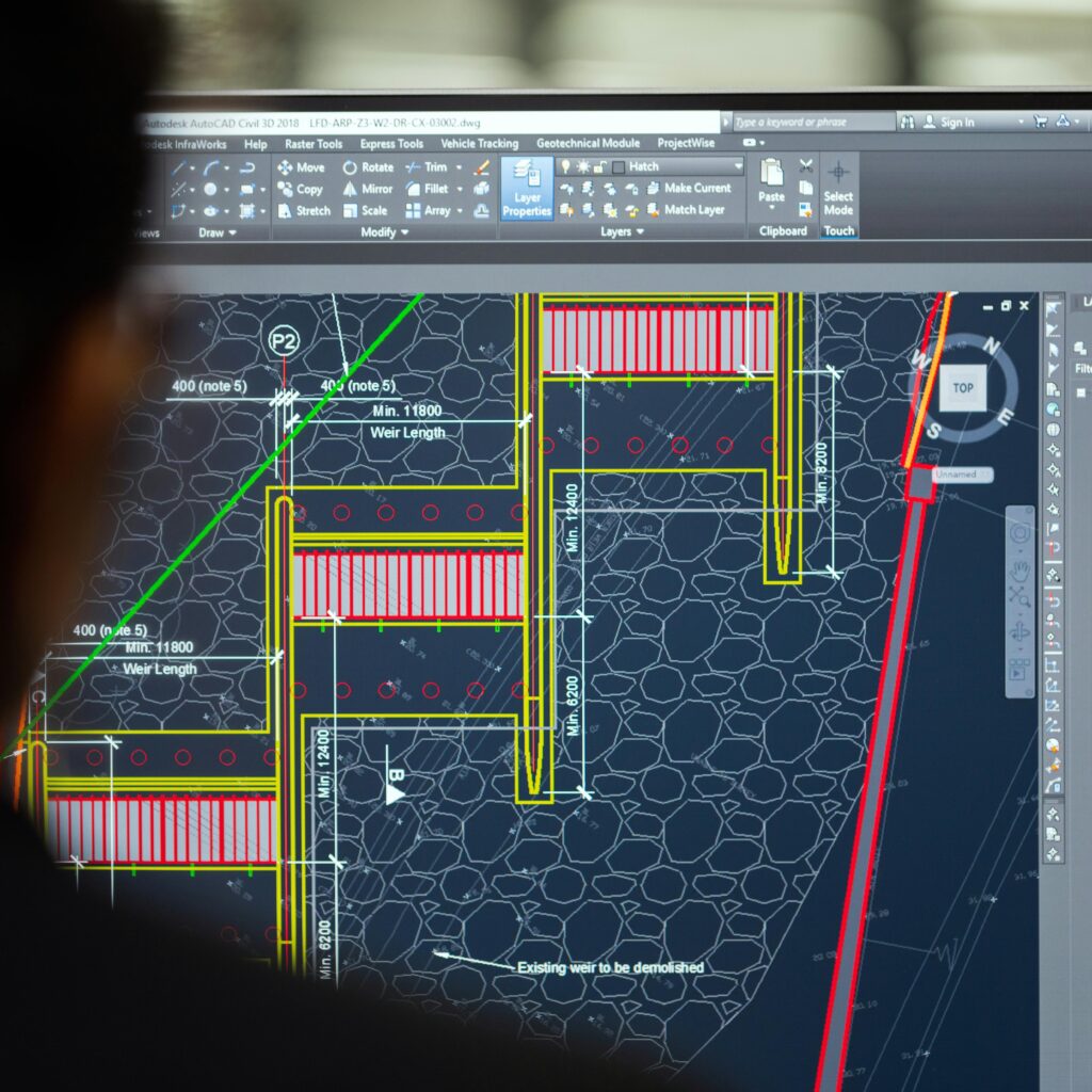 A civil engineer working on a weir design using CAD software on a computer screen in an office setting.