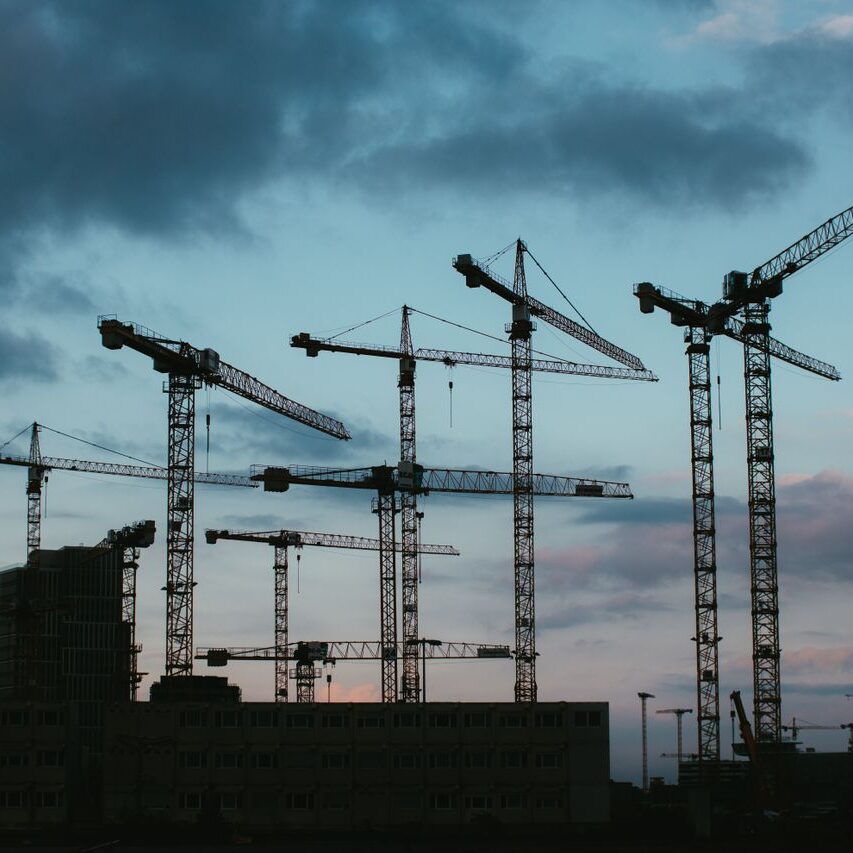 Multiple construction cranes silhouetted against the evening sky, capturing industrial progress.