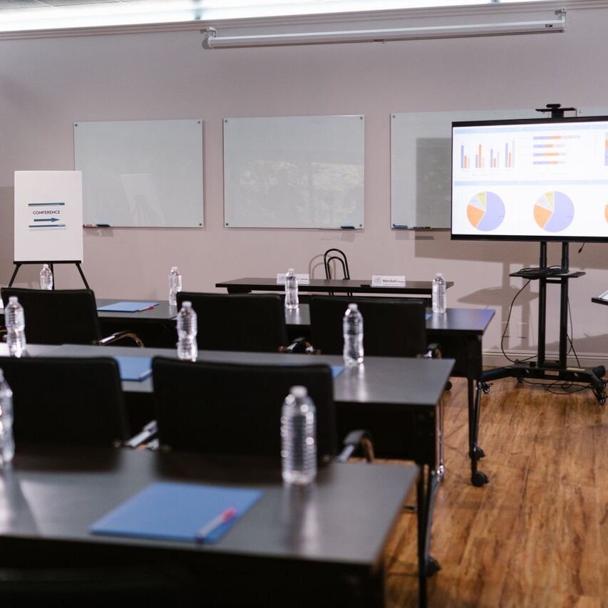 Modern conference room with projector, graphs, chairs, and bottled water setup for presentation.